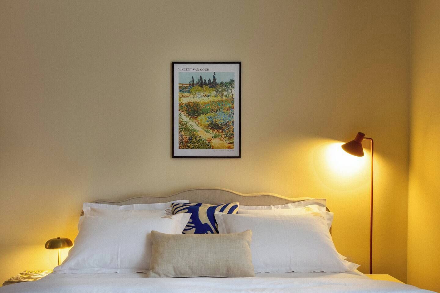 Quarto de hotel com cama, abajur e quadro na parede.