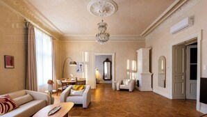 Amplia sala de estar con piso de parquet de madera, un candelabro y una chimenea. Hay varias zonas de estar con sofás y sillones.