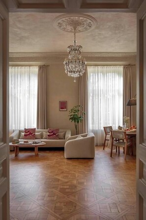 A spacious living room with a chandelier, a sofa, a coffee table, and a dining area with chairs and a table.