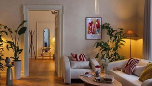 Una sala de estar moderna con un sofá, una mesa de centro y plantas. Hay un cuadro en la pared y una lámpara junto a ella.