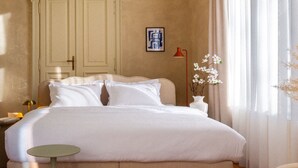 Un dormitorio con una cama grande, una mesita de noche, una lámpara, un jarrón con flores y un cuadro en la pared.