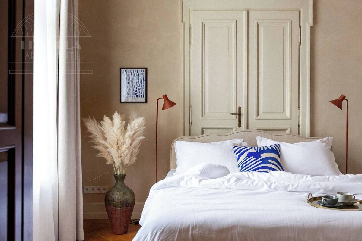 Un dormitorio con cama, un florero con plumas de pampa, un cuadro en la pared y dos lámparas de pie rojas.