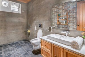 A bathroom with a toilet, sink, and shower. There is a wooden cabinet with a towel and a shelf with toiletries. - Country Ville (Dhanaulti)