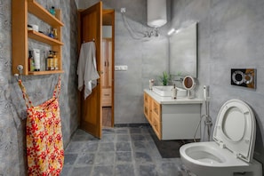 Une salle de bain moderne équipée de toilettes, d’un lavabo et d’étagères où sont rangés les produits de toilette.