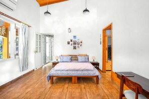 A spacious bedroom with a wooden floor, a large bed with patterned bedding, two bedside tables with lamps, and a wooden wardrobe. - Country Ville (Dhanaulti)