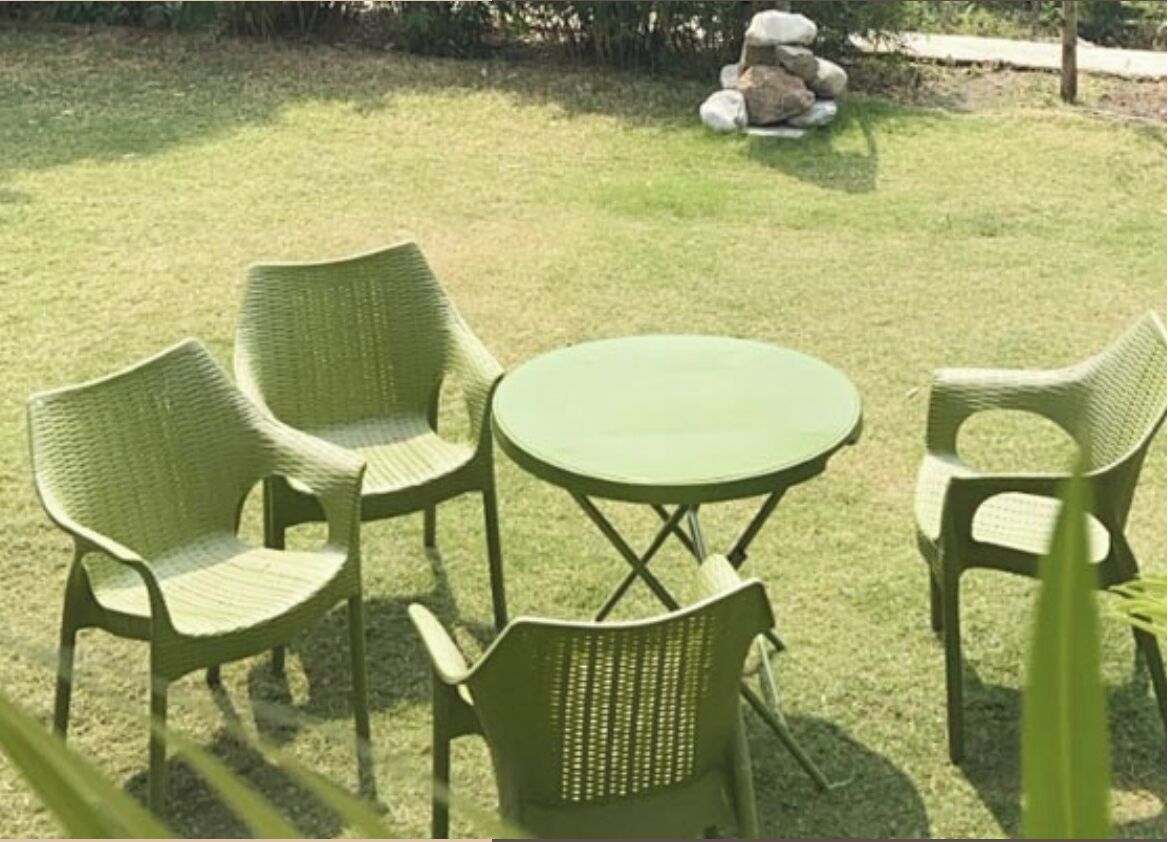 Uma mesa redonda com quatro cadeiras de vime em uma área externa gramada.