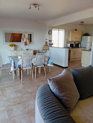 Uma sala de estar aconchegante com um sofá cinzento e uma área de jantar com cadeiras brancas e uma mesa.