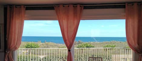Uma varanda com vista para o oceano, uma mesa, cadeiras e um corrimão.