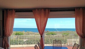 Uma varanda com vista para o oceano, uma mesa, cadeiras e um corrimão.