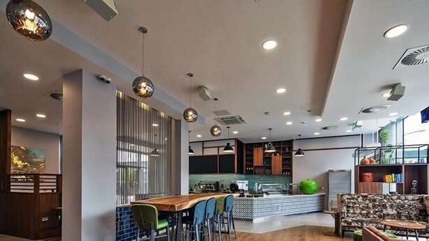 A modern kitchen with a wooden island, bar seating, and a seating area with a patterned sofa. - Liv Student Dublin (Dublin)