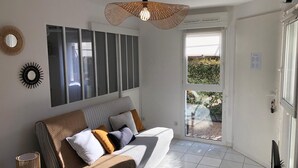 Un salon moderne avec un canapé, un luminaire suspendu et une vue sur l’extérieur.