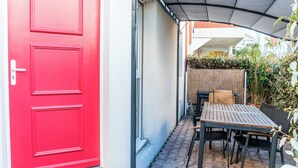Une porte rouge, un patio couvert avec une table et des chaises, et une clôture en bois.