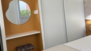 Une chambre à coucher avec un lit, un miroir rond, un petit tabouret et une armoire à porte coulissante.