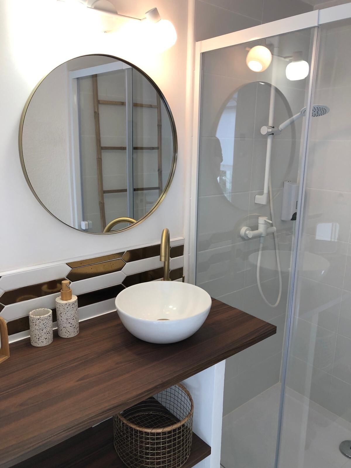 A bathroom with a round mirror, a white vessel sink, and a glass shower enclosure.