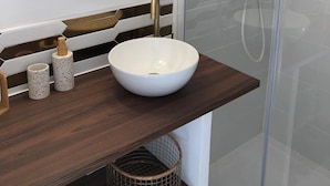 Une salle de bain avec un miroir rond, un lavabo sur colonne blanc et une cabine de douche en verre.