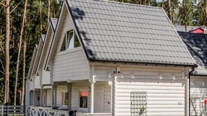 En vit timmerstuga med ett sadeltak, en veranda med vita räcken och en garageport.