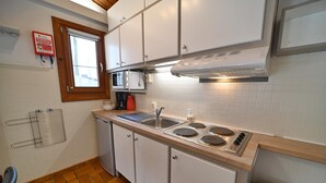 A compact kitchen with white cabinets, a microwave, a stove, and a window with blinds. - Chalet in Viroinval Near Nature Park (Viroinval)