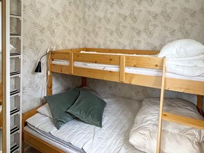 A bunk bed with a wooden frame, a lower bunk with a quilted mattress, and pillows. There is a shelf unit to the left with storage compartments. - 3 Person Holiday Home in Solvesborg (Sölvesborg)