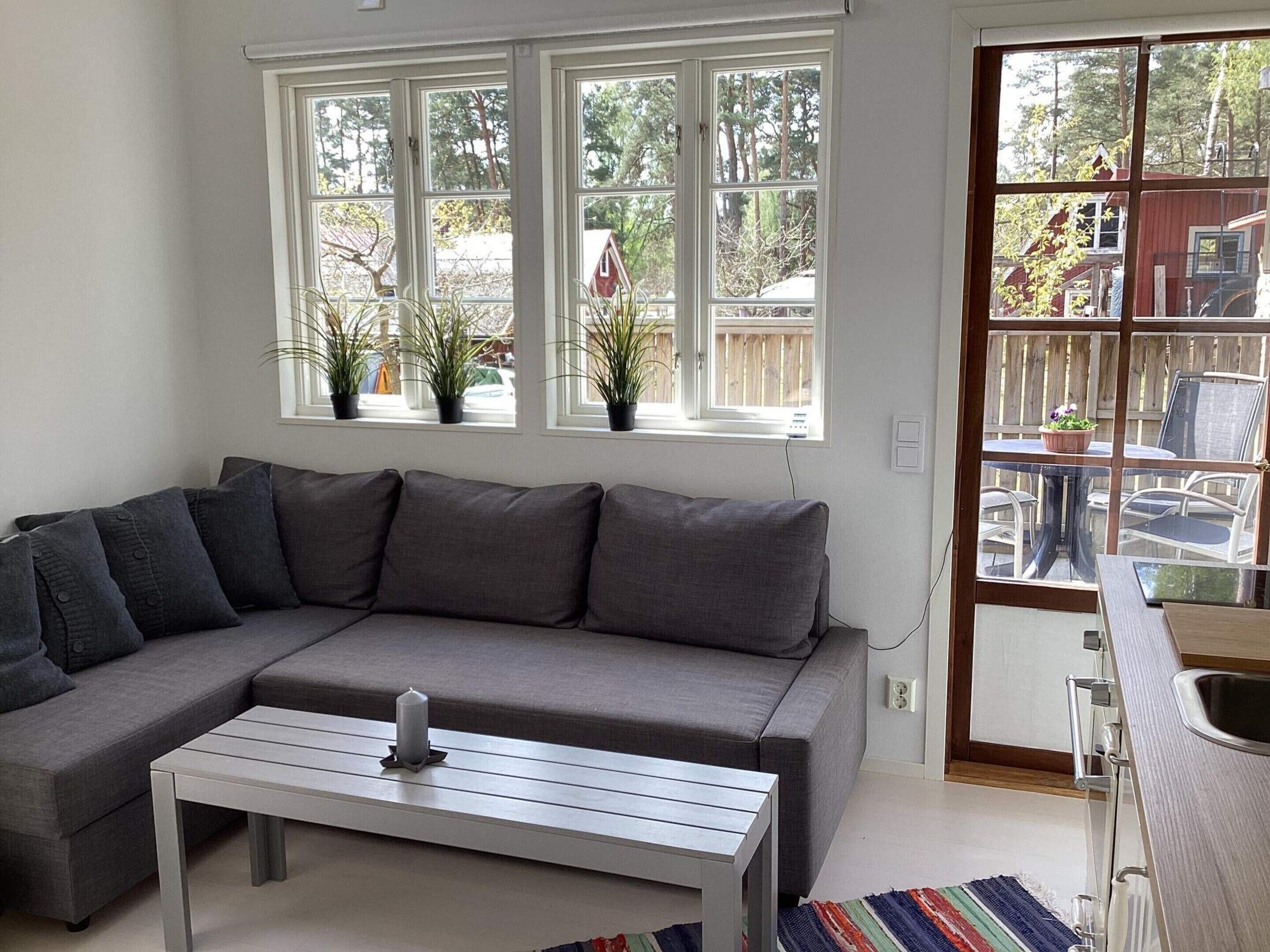 A modern living room with a grey sectional sofa, a white coffee table, and a view of a wooden deck and outdoor furniture through large windows.