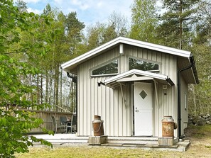 A small, single-story cabin with a gabled roof, a front door, and two large metal containers on the porch. - 3 Person Holiday Home in Solvesborg (Sölvesborg)
