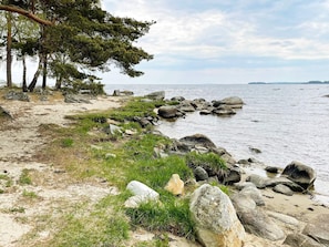 Paisagem costeira com uma praia arenosa, pedras grandes e árvores.
