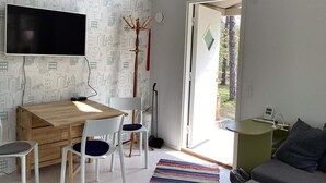 Quarto moderno com escrivaninha de madeira, duas cadeiras brancas, TV fixada na parede e janela com vista para árvores.