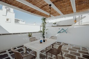A rooftop terrace with a white table and chairs, a hanging light fixture, and a view of buildings in the background. - Casa Lucia in Monopoli (Monopoli)