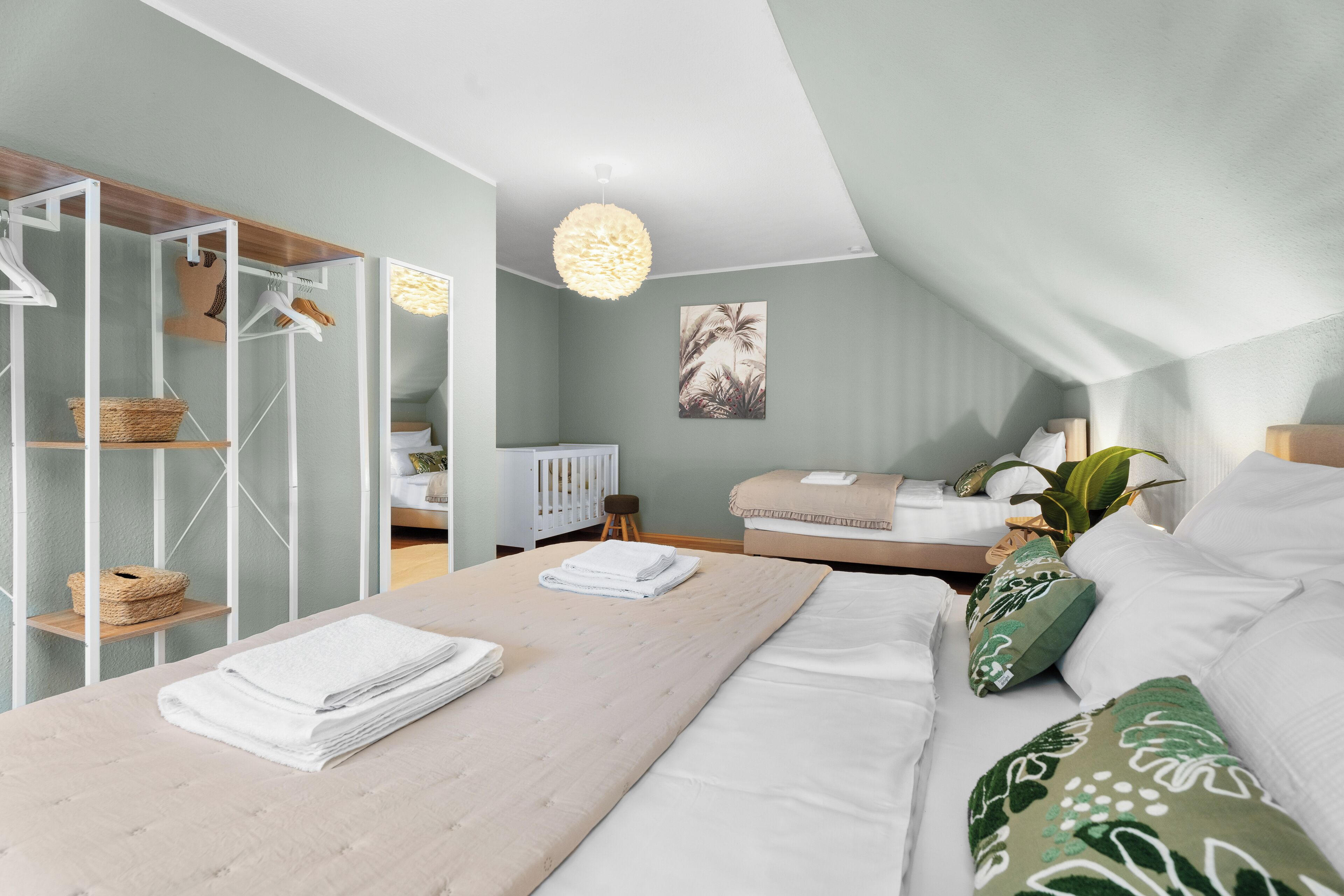 A bedroom with a bed, a bedside table, a hanging light fixture, a crib, and a wardrobe.