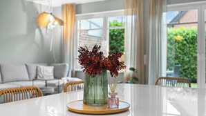 A dining table with a vase of red flowers, a small bottle, and a candle holder.