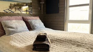 Una cama con cubre cama blanco texturizado, dos almohadas y una pila de toallas dobladas.