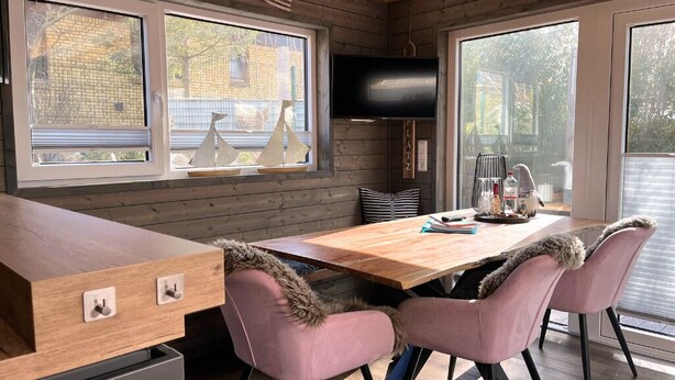 Una cocina moderna con una mesa de madera, sillas rosadas y un televisor encima.