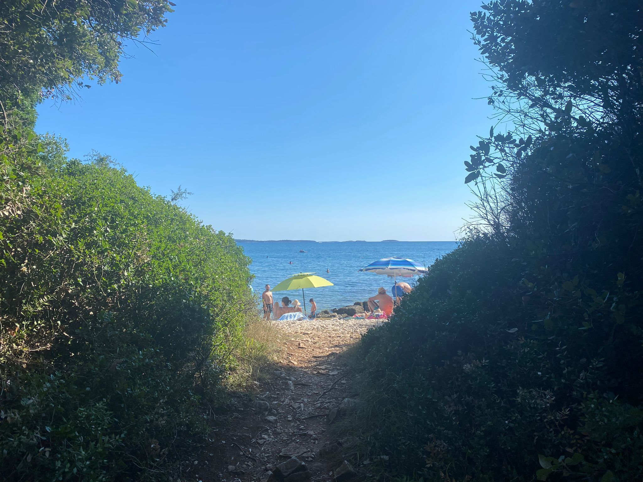 Un camino que lleva a una playa con sombrillas y gente.