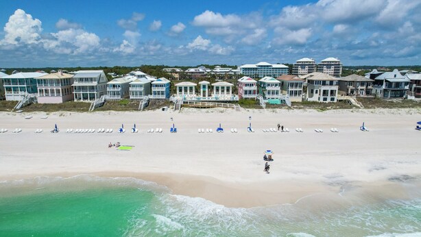 Een strand met wit zand, helder turquoise water en een rij strandhuizen met balkons met uitzicht op de oceaan.
