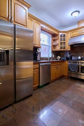 A kitchen with stainless steel appliances, wooden cabinets, a window, and a tiled floor. - Wonderful House in Long Island City, comforting and spacious near to Manhattan (Queens)