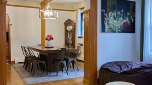 Een eetruimte met een houten tafel en stoelen, een kroonluchter, een klok en een schilderij aan de muur.