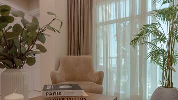 Ein Zimmer mit einem beigefarbenen Sessel, einer weißen Vase mit grünen Blättern und einem Buch mit dem Titel 'Paris' auf einem Tisch.