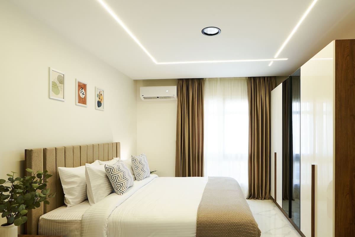 A modern hotel room with a large bed, a bedside plant, a wooden wardrobe, and a large window with curtains.