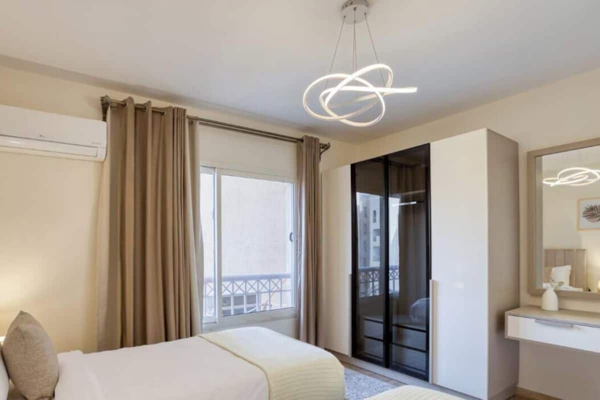 A hotel room with a bed, a bedside table, a mirror, and a window with curtains.