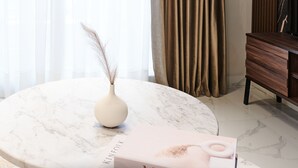 Une table en marbre avec un vase et une boîte portant l’inscription « KINEOIK », dans une pièce décorée de rideaux et comprenant un meuble en bois.