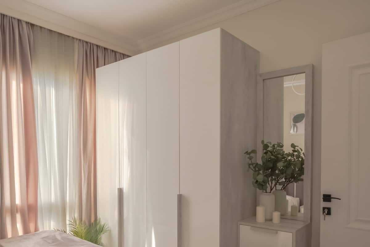 A bedroom with a bed, a wardrobe, a mirror, and a nightstand with a plant.