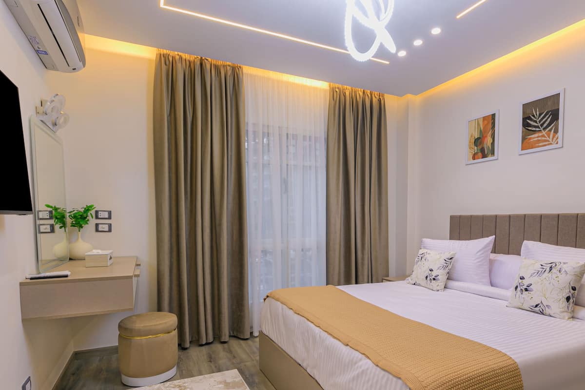 A modern hotel room with a large bed, a bedside table with a lamp, a mirror, and a wall-mounted air conditioner.