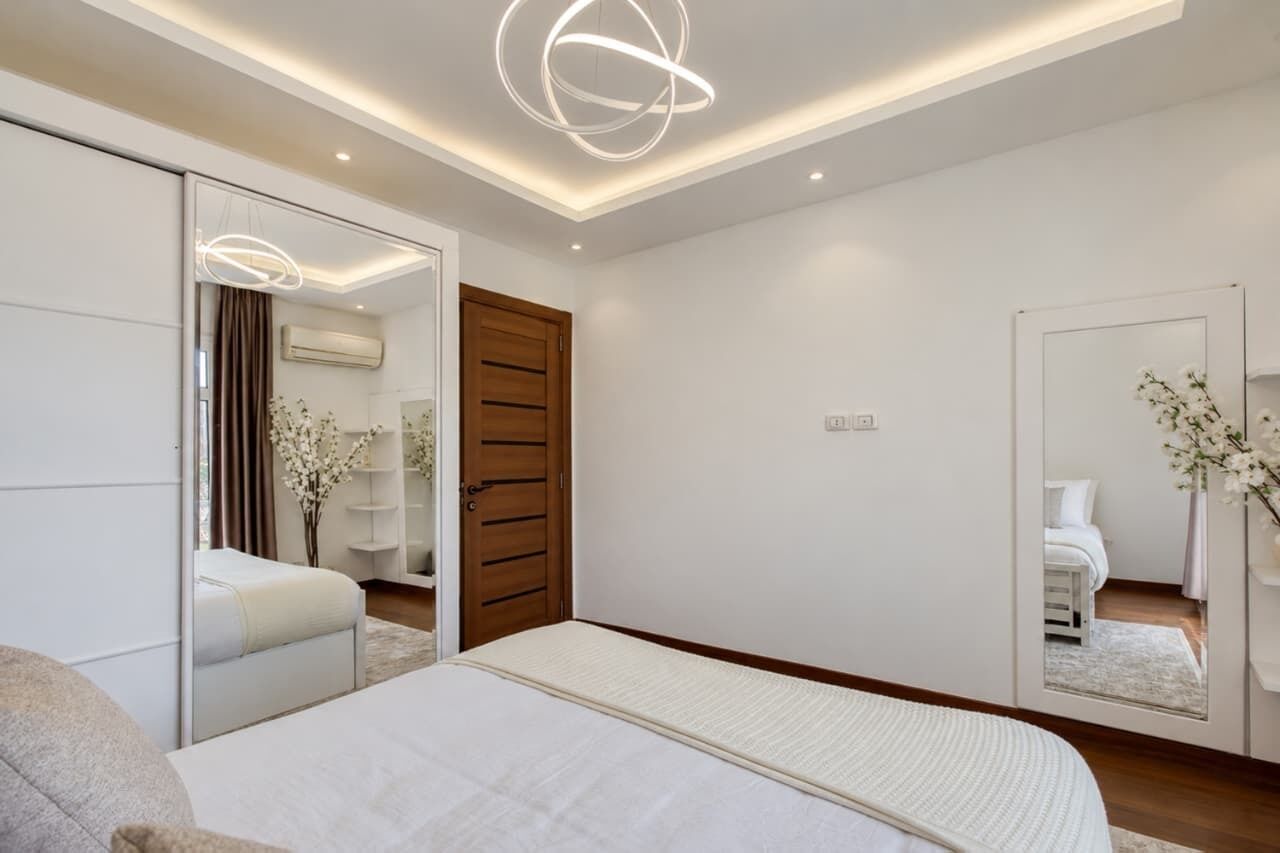 Ein modernes Schlafzimmer mit Bett, Kleiderschrank, Spiegel und Deckenleuchte.