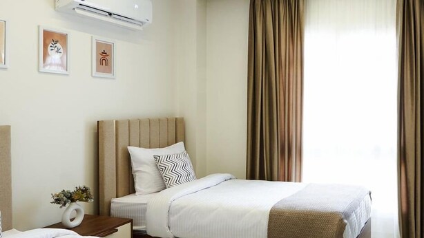 Une chambre d’hôtel avec deux lits, une table de chevet ornée d’un vase de fleurs et un climatiseur fixé au mur.