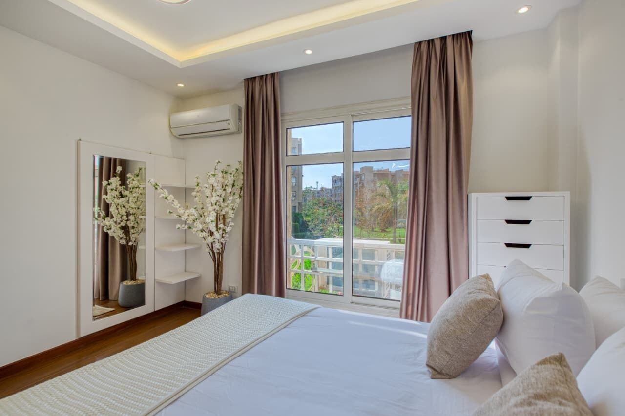 A bedroom with a large bed, a wardrobe, a mirror, and a window with curtains.