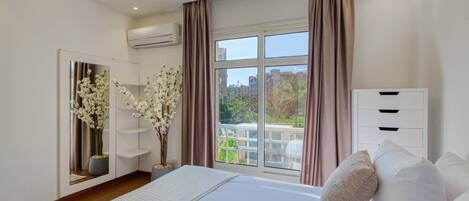 A bedroom with a large bed, a wardrobe, a mirror, and a window with curtains.