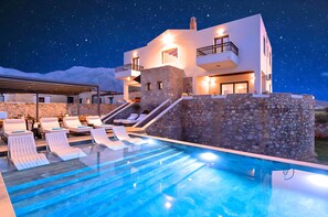 A modern hotel with a pool, stone walls, and a starry night sky.