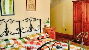 Un dormitorio con estructura de cama metálica, mesita de noche de madera, lámpara verde y armario rojo.