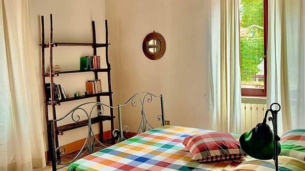 Un dormitorio con cama, una estantería y una ventana con cortinas.