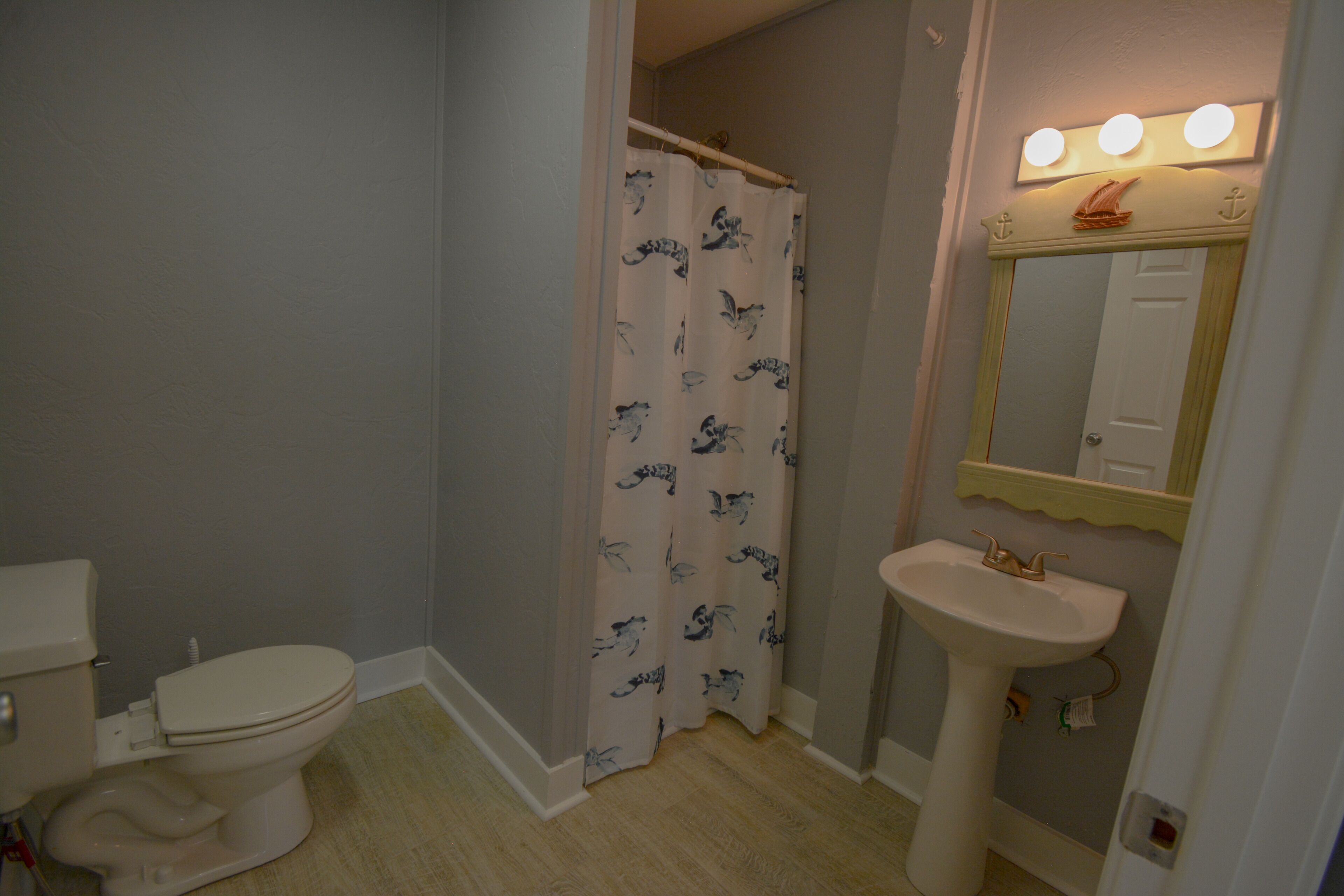 A bathroom with a toilet, a shower curtain, a sink, and a mirror with lights.