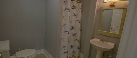 A bathroom with a toilet, a shower curtain, a sink, and a mirror with lights.